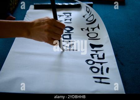 Ulsan, South Korea - October 5, 2024: A close-up of a hand using a traditional brush to practice Korean calligraphy on paper, creating expressive stro Stock Photo