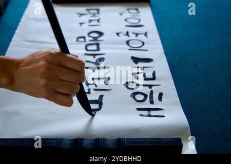 Ulsan, South Korea - October 5, 2024: A close-up of a hand using a traditional brush to practice Korean calligraphy on paper, creating expressive stro Stock Photo