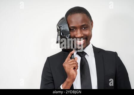 African young man wearing black suit taking off plastic mask revealing face and smiling Stock Photo