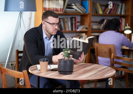 Man reading book and drinking coffee in a cafe with many books on a background Stock Photo
