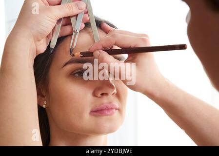 Changing the shape of the brows. Stylist measuring the eyebrows with the ruler. Micropigmentation work flow in a beauty salon. Woman having her eye br Stock Photo