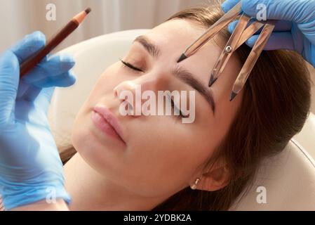 Changing the shape of the brows. Stylist measuring the eyebrows with the ruler. Micropigmentation work flow in a beauty salon. Woman having her eye br Stock Photo