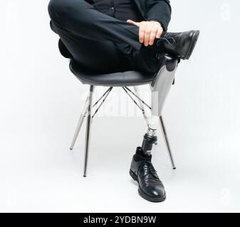 Cropped view of disabled young man with prosthetic leg sitting on a chair in studio, artificial limb concept over white backgrou Stock Photo