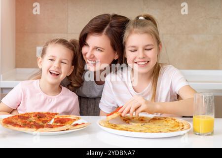 Mother and two daughters eating homemade pizza at a table in kitchen, happy family concept Stock Photo