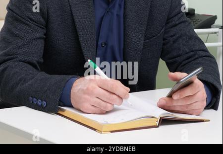 Mature man sitting in his office writing in notepad Stock Photo