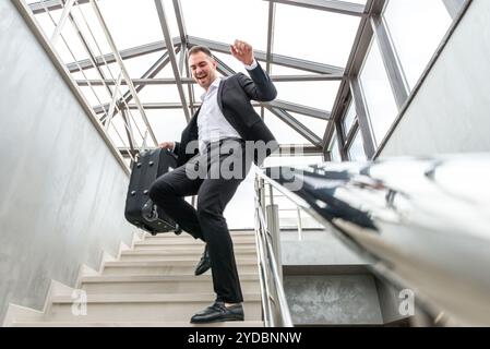 Happy businessman wearing formal suit sliding on stairs Railing in modern business building. Hurry and freedom concept Stock Photo