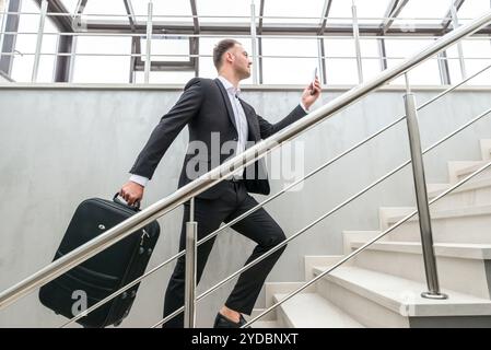 Businessman holding suitcase running on stairs in modern building Stock Photo