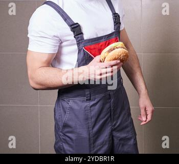 Cropped view of worker wearing uniform eating burger during lunch break Stock Photo