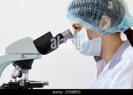 Female scientist looking through microscope in modern chemical laboratory doing some research. Analyzing samples using a microsc Stock Photo