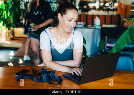 Confident beautiful middle aged woman photographer sitting in stylish modern cafe with laptop and camera. Stock Photo