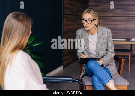 Portrait of a female psychotherapist listening attentively to a woman client at a session in an office. Stock Photo