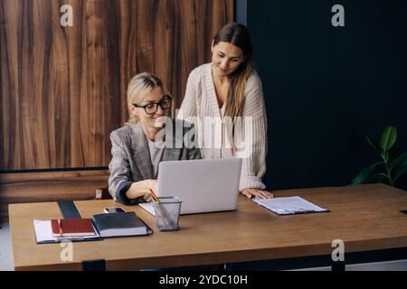 Two positive young women working and discussing together at office table coworking. Stock Photo