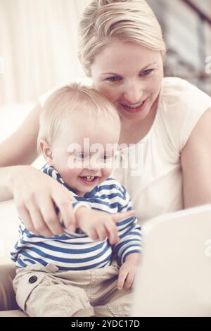 Woman, baby and happy on sofa with tech, entertainment or child favorite cartoon in home. Mother, toddler or tablet in living room for streaming Stock Photo