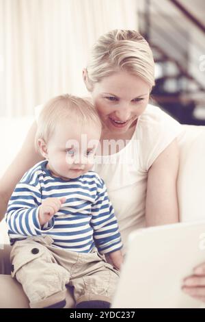 Mother, baby and happy on sofa with tech, entertainment or child favorite cartoon in home. Woman, toddler or tablet in living room for streaming Stock Photo