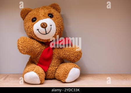Plush Teddy Bear wearing a Red Bow resting on a lovely shelf for display Stock Photo