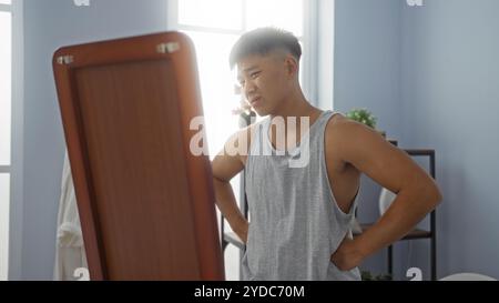 Handsome young man in spa wellness center examining himself in a mirror with a focused expression in a modern indoor setting Stock Photo