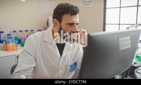 Concentrated middle-aged bearded man in lab coat working indoors at hospital computer. Stock Photo
