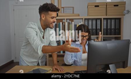 Young man and woman collaborating enthusiastically in a modern office with bookshelves and files in the background Stock Photo