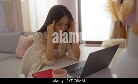 Young woman looking stressed with hands on head while using laptop in living room at home in china. Stock Photo