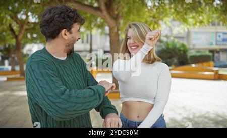 A joyful couple enjoys a dance move together in a lush urban park, displaying love and happiness Stock Photo