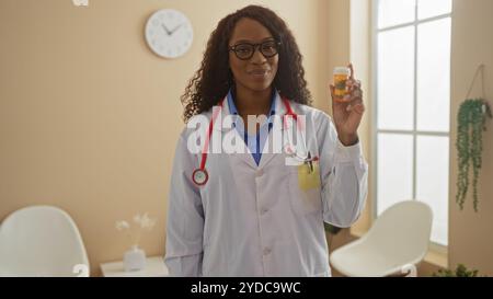 A young african american woman doctor in a clinic holding a prescription bottle, showcasing healthcare professionalism indoors. Stock Photo