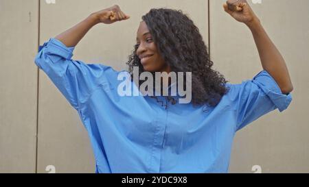 Happy, strong, african american woman with curly hair wearing a blue shirt poses confidently against an isolated white background, displaying empowerm Stock Photo