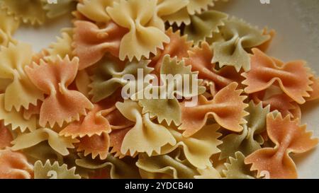 Colorful farfalle pasta close-up showcasing the texture and pattern of the bow-tie-shaped noodles in various shades of red, green, and yellow. Stock Photo