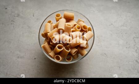 Dry pasta in a clear glass bowl on a gray kitchen countertop shot from above Stock Photo