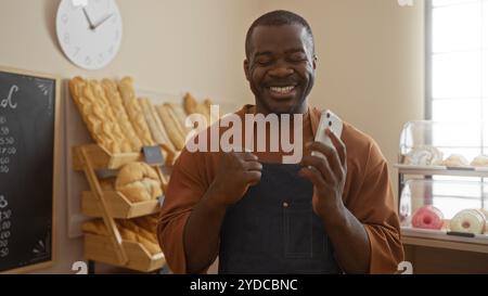 Smiling man holding phone in bakery shop with bread in background Stock Photo
