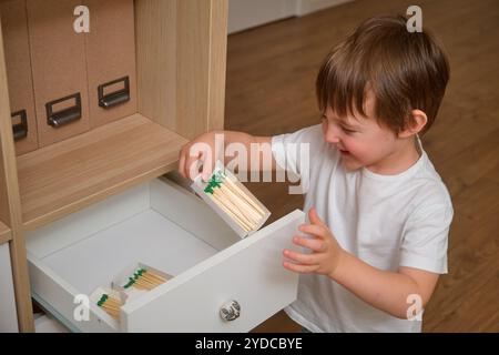 The child is playing with matches indoors, unaware of the danger. A toddler baby holds a matchstick at home, creating a risky situation. Kid aged 3 ye Stock Photo