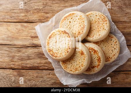 Fresh from the oven English Crumpets or porous bread close-up on parchment on an old table. Horizontal top view from above Stock Photo