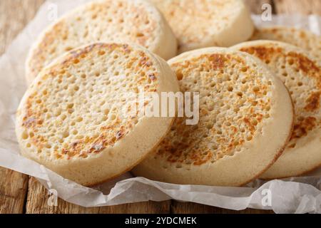 Fresh from the oven English Crumpets or porous bread close-up on parchment on an old table. Horizontal Stock Photo