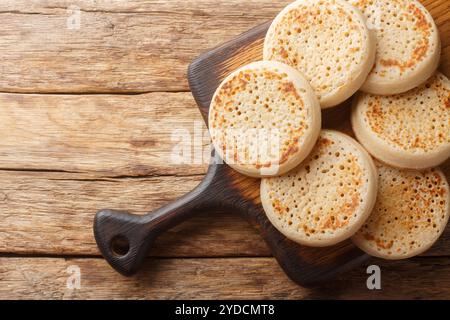 Close up of fresh golden crumpets on the wooden board on the table. Horizontal top view from above Stock Photo
