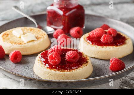 Hot Toasted Crumpets with piece of butter and raspberry jam closeup on the plate on the table. Horizontal Stock Photo