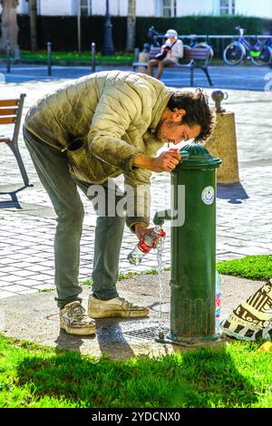 Unemployed and unhoused vagrant pouring water from public tap into plastic bottles - Tours, Indre-et-Loire (37), France. Stock Photo