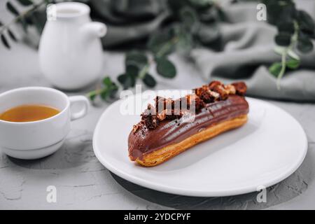 Eclair with Chocolate Cream and Hazelnuts and tea Stock Photo