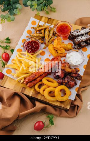 French fries potatoes with onion rings, sausages, croutons and spicy chicken legs Stock Photo