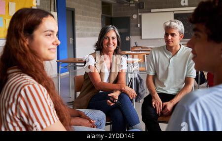 Portrait of a mature female teacher looking at camera, sitting in circle with university students. Stock Photo