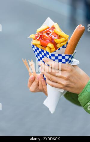 Female hands holding paper cone with a hot sausage and french fries with ketchup Stock Photo