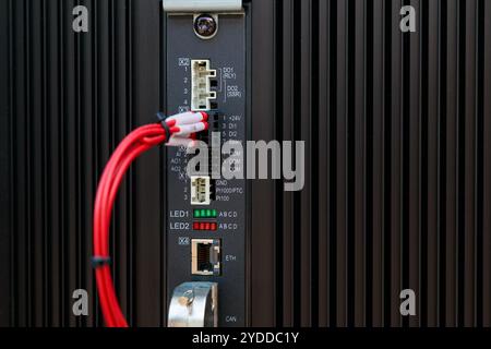 Red cable connecting to input output module of a programmable logic controller with visible leds and communication ports Stock Photo