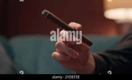 Close up unknown successful Caucasian man guy unrecognizable rich businessman male hand holding cigar smoking tipped cigarette ash home living room Stock Photo