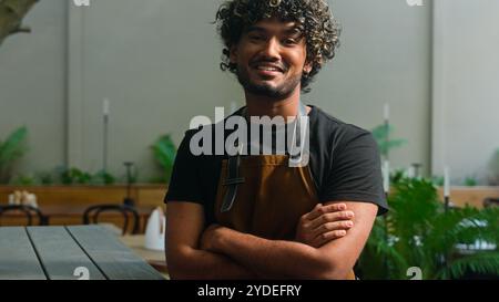Confident smiling happy Latino American ethnic male glad man cafe worker in apron guy waiter cleaner barista small business owner crossing hands Stock Photo