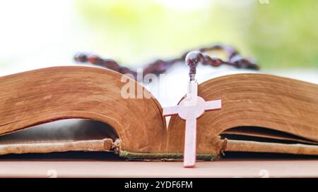 Dark red copper cross leaning against an old open book symbolizing the spread of Jesus Christs love among Christians reflecting faith devotion and the Stock Photo