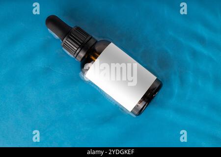 Amber Dropper Bottle on Blue Water Surface with Blank Label Stock Photo