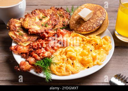 Full American Breakfast with scrambled eggs, fried bacon, hash browns and pancakes on plate close up with coffee and juice. Stock Photo