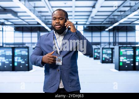 Businessman talking on phone in high tech data center housing advanced computing equipment. African american man delegating tasks in technologically advanced environment during telephone call Stock Photo