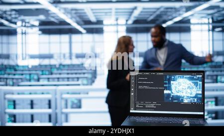 Close up of laptop with AI technology used to sustain data center hardware. Focus on notebook used by server room programmers in background using artificial intelligence tech, camera B Stock Photo