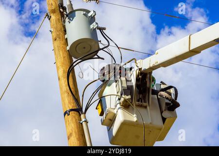 Bucket truck supports worker attending to electrical infrastructure on pole after hurricane Stock Photo