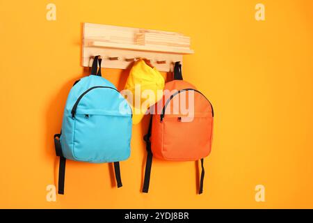 Bright backpacks and cap hanging on orange wall Stock Photo