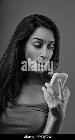 Black and white portrait of a surprised young woman reading shocking news on a smartphone, expressing astonishment and disbelief Stock Photo
